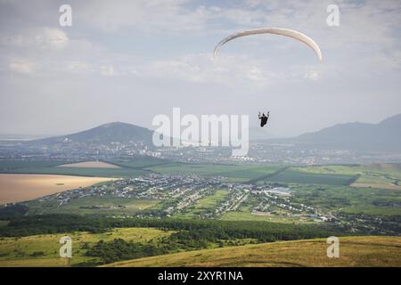 Il parapendio professionista in una tuta da cocco vola in alto sopra il terreno contro il cielo e i campi con le montagne Foto Stock