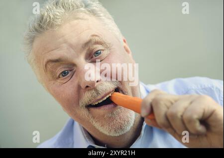 Un cittadino anziano mangia una carota con piacere Foto Stock