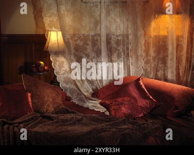 Camera da letto con luce soffusa, letto rosso scuro e due lampade. Impostazioni interne Foto Stock