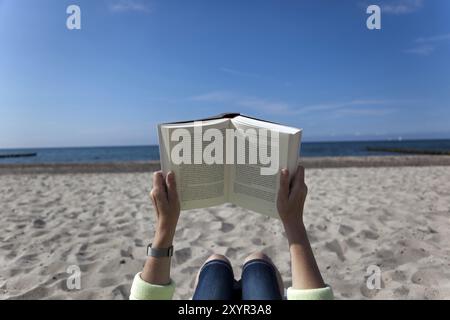 Villeggiante sdraiato sulla spiaggia a leggere un libro Foto Stock