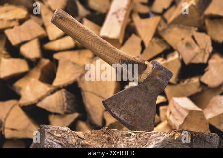 L'ascia è bloccata in un tronco sullo sfondo di legna da ardere tritata giacente in un piolo piatto. Primo piano Foto Stock