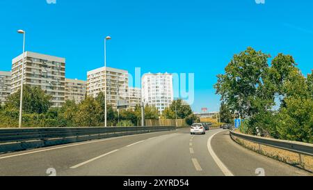 Lisbona, Portogallo, 3 agosto 2024. Le auto viaggiano lungo una strada con alti appartamenti e vegetazione sullo sfondo. Foto Stock