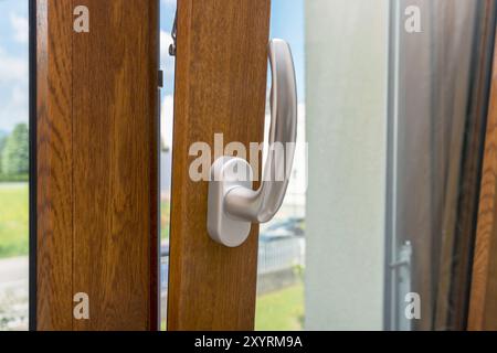 Finestra in legno con dettagli aperti. Finestra inferiore appesa. Vista ravvicinata del telaio della porta in legno, metallo, PVC. Elegante impugnatura cromata. Efficienza energetica e profilo di sicurezza. Foto Stock