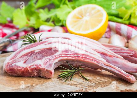 Costolette di agnello crudo con spezie ed erbe da vicino su sfondo di legno Foto Stock