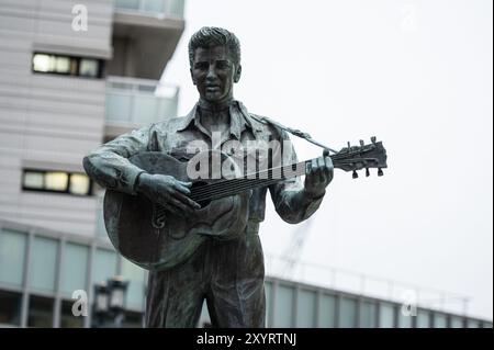 Una statua in bronzo del musicista Elvis Presley che suona una chitarra, catturata in un ambiente urbano. La statua, decorata con un abbigliamento classico, si erge così Foto Stock