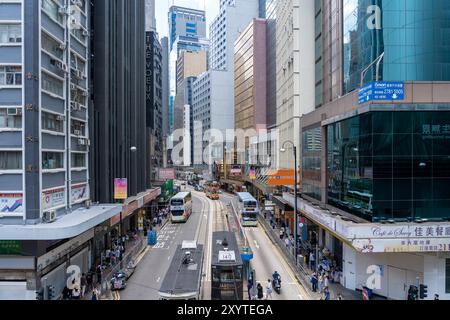 Hong Kong, Cina - 3 luglio 2024: Una strada trafficata di Hong Kong, in Cina, con edifici alti che costeggiano la strada. Ci sono molte persone che camminano e auto dri Foto Stock