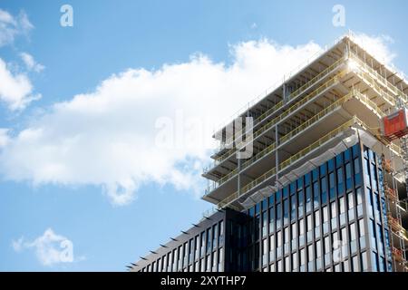 Sito di costruzione di un moderno grattacielo con facciata in vetro con una gru sullo sfondo del cielo limpido, che costruisce l'edificio degli uffici di Sickla Central Foto Stock