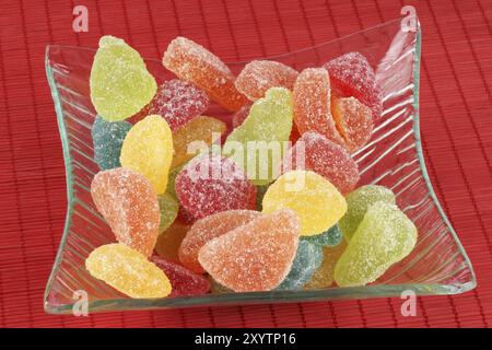 Frutta Assortiti sagomata e aromatizzati gelatine in maniera trasparente del contenitore in vetro su uno sfondo rosso Foto Stock