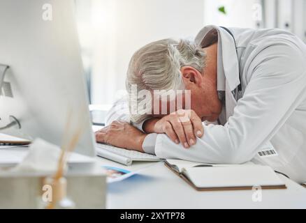 Uomo maturo, medico e che dorme sulla scrivania dopo il burnout, il lavoro eccessivo o l'insonnia in ufficio. Stanco maschio medico professionale, computer e pisolino per il riposo Foto Stock