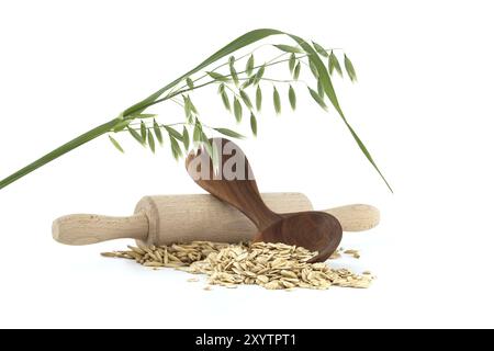 Semole di avena arrotolate e appiattite in scaglie in cucchiaio di legno e chicchi di avena con carene o bucce vicino a matterie di legno isolate su fondo bianco Foto Stock