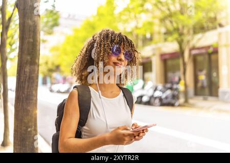 Vista laterale primo piano con ritratto dello spazio di copia di una donna allegra latina che ascolta musica al telefono per strada Foto Stock