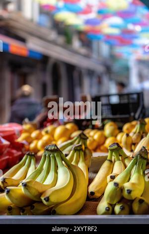 Banane fresche in mostra in un vivace mercato della frutta di Catania, con uno sfondo di ombrelli colorati che creano un vivace baldacchino. Cattura l'essenza di si Foto Stock