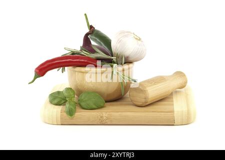 Peperoncini in mortaio di legno, cipolla rossa, pepe nero, rametto di basilico e bulbo d'aglio isolato su fondo bianco. Spezie, erbe e tema aromatizzante s Foto Stock