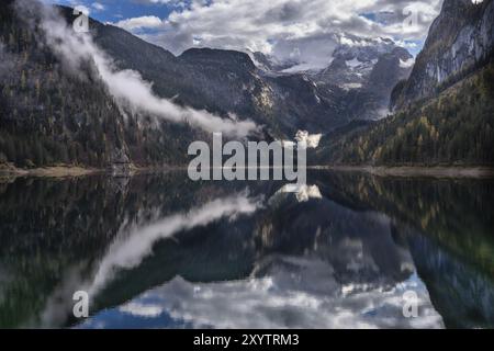 Il Vordere Gosausee in autunno. Sullo sfondo, la catena montuosa del Dachstein è caratterizzata da nuvole. Cielo e sole in parte blu. Foresta nuvolosa. Vorderer Gosausee, Foto Stock