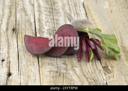 Barbabietola cruda tagliata e intera con foglie verdi su fondo grigio rustico in legno Foto Stock