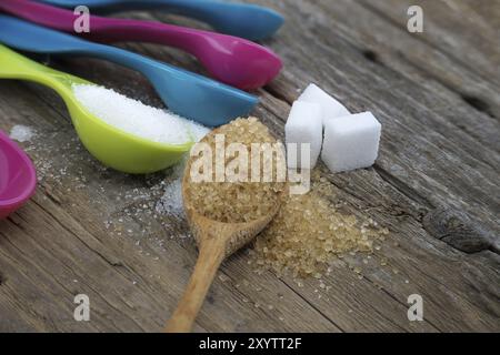 Zucchero di canna di canna di canna e zucchero bianco in colorati misurini di plastica versati su una superficie rustica in legno, misurando utensili in setti da cucina Foto Stock