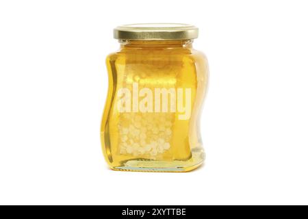 Un vaso di vetro con coperchio dorato contiene miele con favo riempito quasi fino in cima, su sfondo bianco Foto Stock