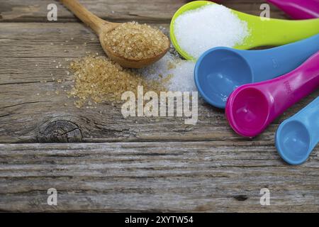 Set di misurini colorati in plastica con zucchero di canna e zucchero bianco versato su una superficie rustica in legno Foto Stock