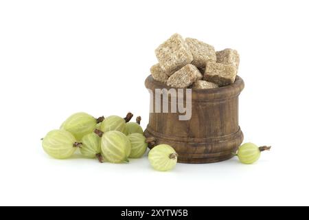 Uva spina verde matura accanto ai cubetti di zucchero di canna in un recipiente di legno, per la conservazione degli alimenti Foto Stock