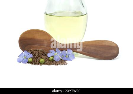 Cucchiaio di legno ripieno di piccoli semi di lino marrone e fiori di pianta di lino blu insieme all'olio di lino in decanter di vetro isolato su fondo bianco Foto Stock