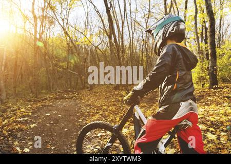 Ritratto di un giovane pilota in piena protezione di una maschera integrale casco e guanti su una bicicletta in una foresta autunnale con foglie gialle. Il concetto di Foto Stock