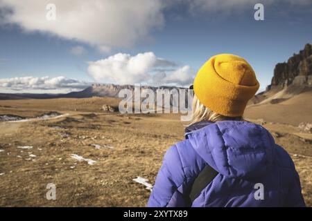 Primo piano Ritratto dal retro di una ragazza viaggiatrice in una giacca con un cappello e uno zaino si staglia sullo sfondo di un paesaggio epico con rocce Foto Stock