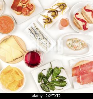 Tapas spagnoli, overhead square shot. Vino, sardine, insalata russa, padron peperoni, jamon e altri snack, ripresa dall'alto su sfondo bianco Foto Stock