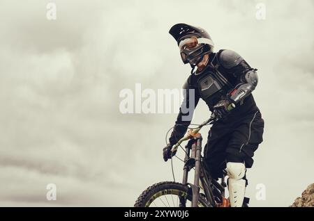 Guida professionista in discesa in mountain bike lungo la collina sullo sfondo della catena montuosa e la tempesta che si avvicina al tramonto Extr Foto Stock