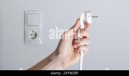 Spina bianca con cavo nella mano di uomini, pronta per il collegamento. Concetto energetico Foto Stock