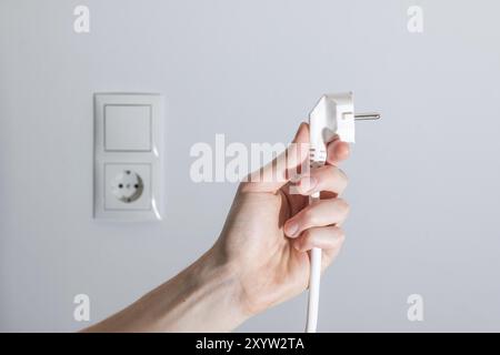 Spina bianca con cavo nella mano di uomini, pronta per il collegamento. Concetto energetico Foto Stock