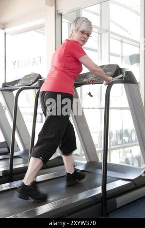 Donna, più di 50 anni, che si allena sul tapis roulant in un centro fitness Foto Stock