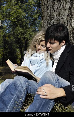 Coppia, giovane uomo e donna, seduti sotto un albero in mezzo alla natura a leggere un libro Foto Stock