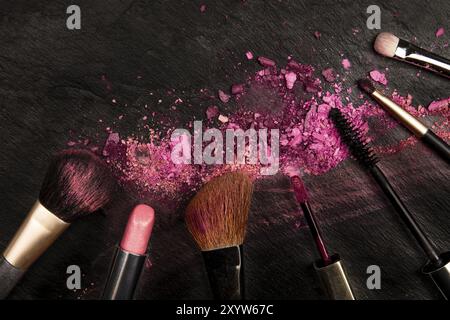 Make-up pennelli e rossetto con cosmetici frantumato, overhead shot su uno sfondo nero con copia spazio, una bellezza modello di progettazione per un banner per il trucco Foto Stock