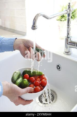 Immagine ritagliata della donna lavare i pomodori e cetrioli in cucina. Le mani nel fuoco Foto Stock