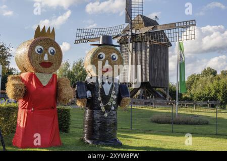 Due grandi uomini di paglia, uno con un vestito rosso e uno con una giacca da cena, si stagliano in un prato di fronte a un mulino a vento, Weseke, muensterland, germania Foto Stock