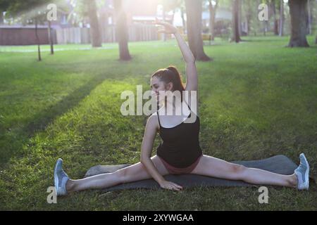 Donna che si allunga in un esercizio all'aperto sorridente felice facendo stretching dopo la corsa. Splendido modello sportivo sorridente all'aperto al tramonto d'estate Foto Stock