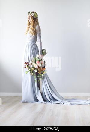 Primavera di bellezza ritratto di una sposa con una ghirlanda e un mazzo di fiori in mano con il muro grigio Foto Stock