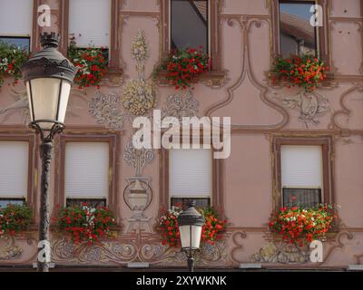 Facciata decorata con decorazioni elaborate e fiori sotto le finestre accanto a un lampione, Weissenburg, Alsazia, Francia, Europa Foto Stock