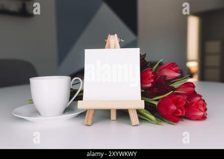 Bouquet di tulipani rossi sul tavolo e tazza di caffè bianco, cornice bianca vuota. Concetto per biglietto d'auguri. Concetto di giorno delle madri, giorno internazionale delle donne co Foto Stock
