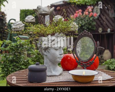 Primo piano di un tavolo decorativo in giardino con busto, specchio e fiori, atmosfera rustica, borken, muensterland, germania Foto Stock