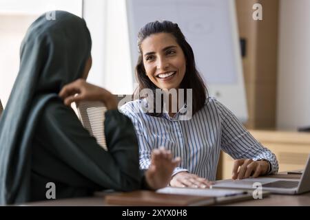 Donna professionale ispanica positiva che parla con una collega araba Foto Stock