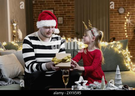 Buon Natale e Felice Anno Nuovo. Sorpresa regalo. Una ragazza sorridente piccola felice apre un regalo di Natale in stupore. Padre dà il suo malessere Foto Stock