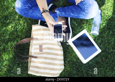 Telefono cellulare in una mano della ragazza su uno sfondo di erba verde Foto Stock