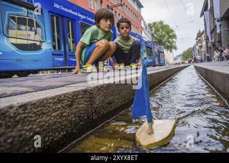 Ninos jugando con un barquito de madera en los canales de agua, Muensterplattz, Friburgo de Brisgovia, Germania, Europa Foto Stock