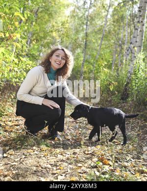 Giovane donna che gioca con il cucciolo nero labrador retriever nella foresta autunnale Foto Stock