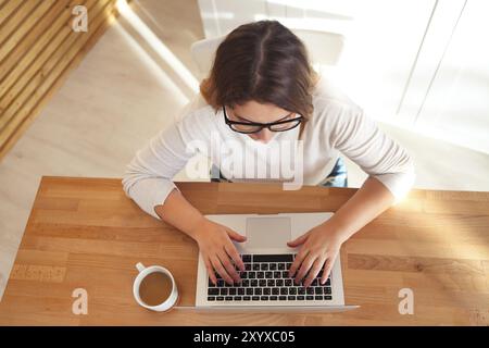 Vista dall'alto di womans mani digitando sulla tastiera del notebook con gli occhiali e il caffè sul tavolo. Mock up minimo piatto eroe laico la testata Foto Stock