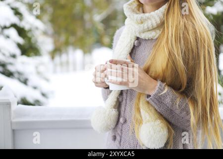 Giovane e bella donna con capelli biondi all'aperto e tazza di caffè caldo con maglione caldo lavorato a maglia. Concetto di comfort invernale Foto Stock