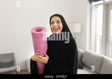 Felice allegra giovane donna araba che tiene il tappetino da yoga arrotolato Foto Stock