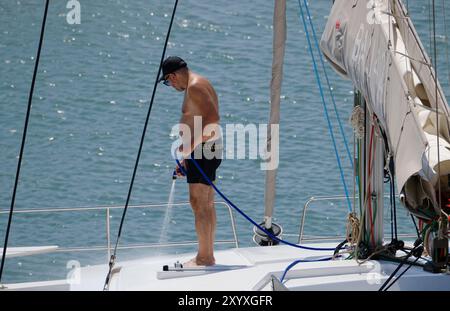 Italia, Sicilia, Mar Mediterraneo, Marina di Ragusa (provincia di Ragusa); uomo che pulisce un catamarano a vela nel porto Foto Stock