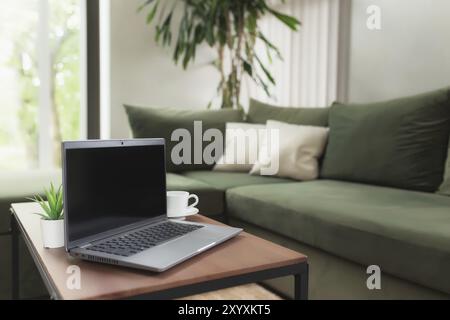 Lavoro da casa, spazio di lavoro, desktop, concetto di lavoro remoto, computer portatile grigio sottile schermo nero vuoto su tavolo di legno marrone con tazza di caffè bianco, Foto Stock